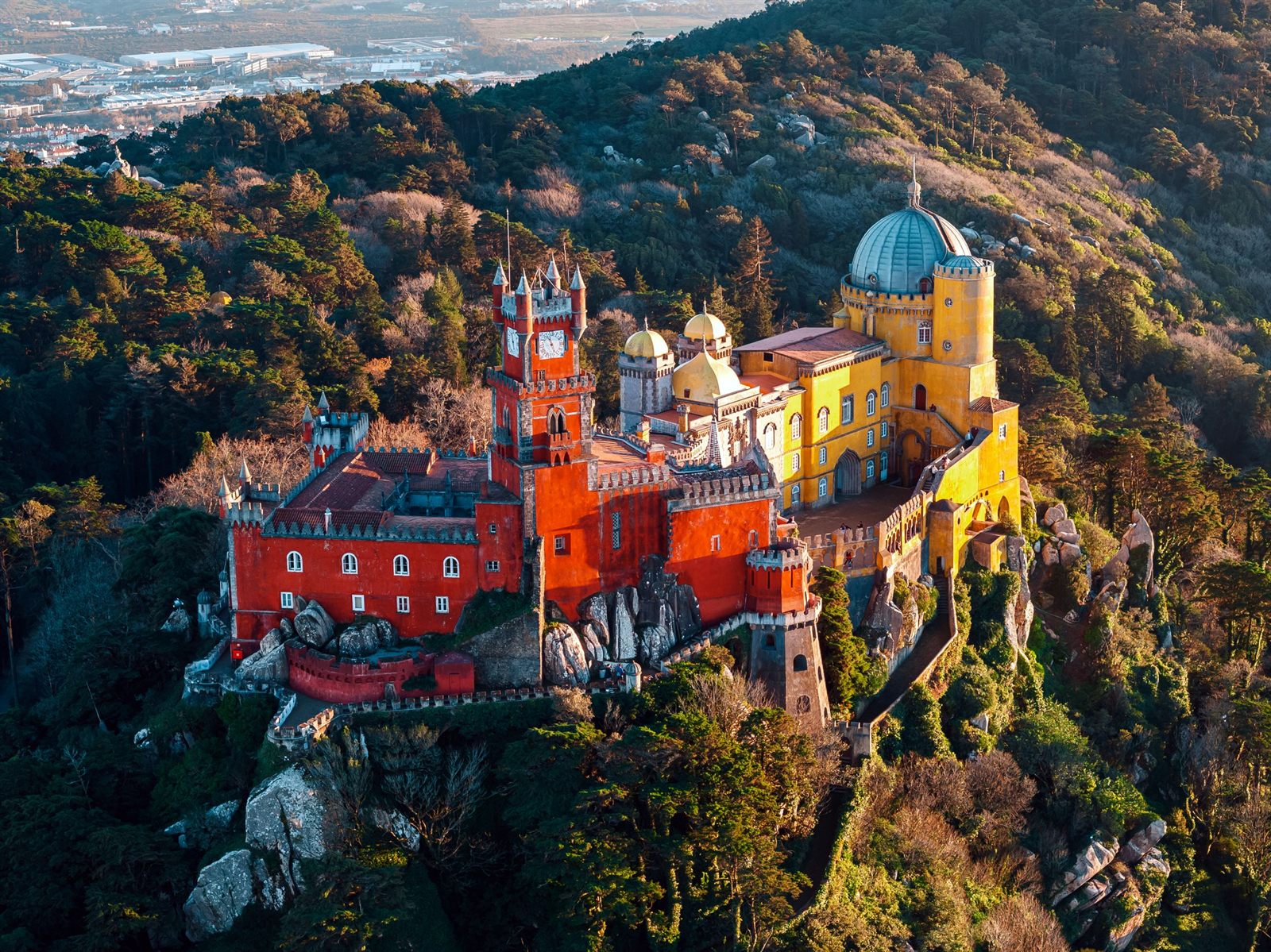 Colorful hilltop palace surrounded by forest at sunset in Sintra